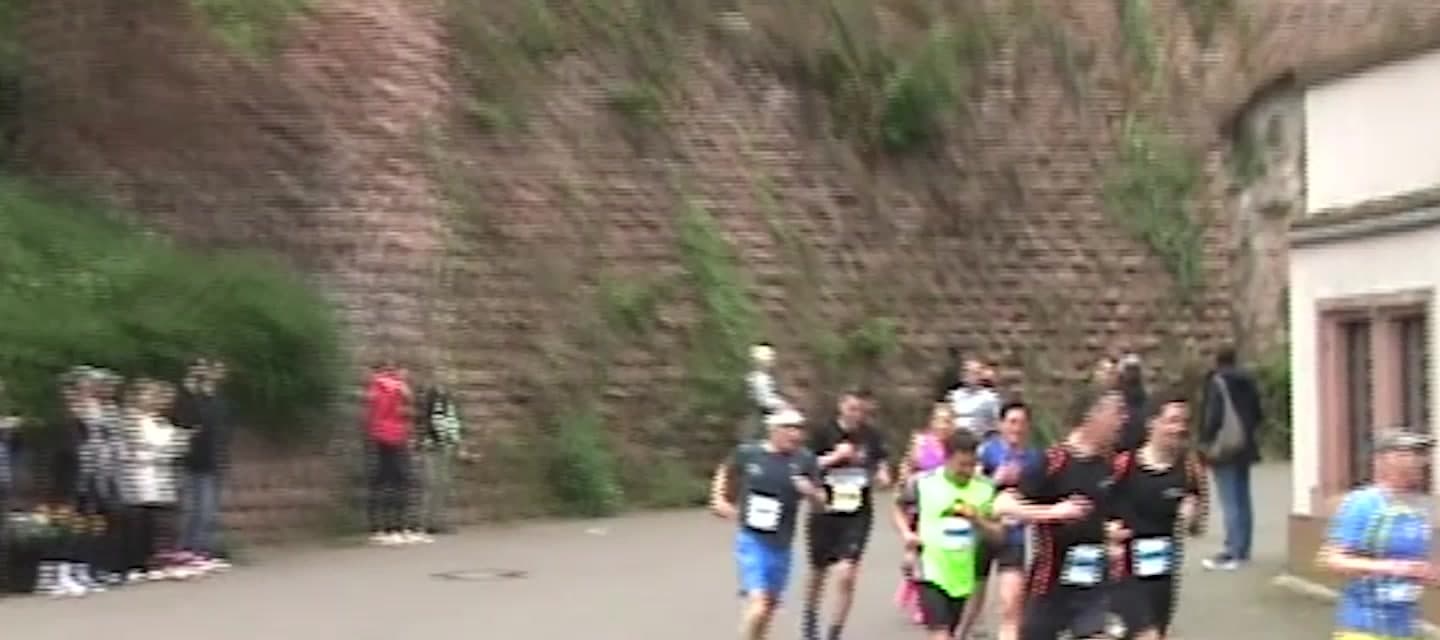 Läuferinnen und Läufer mit Startnummern bei einem Stadtlauf vor einer Bruchsteinmauer