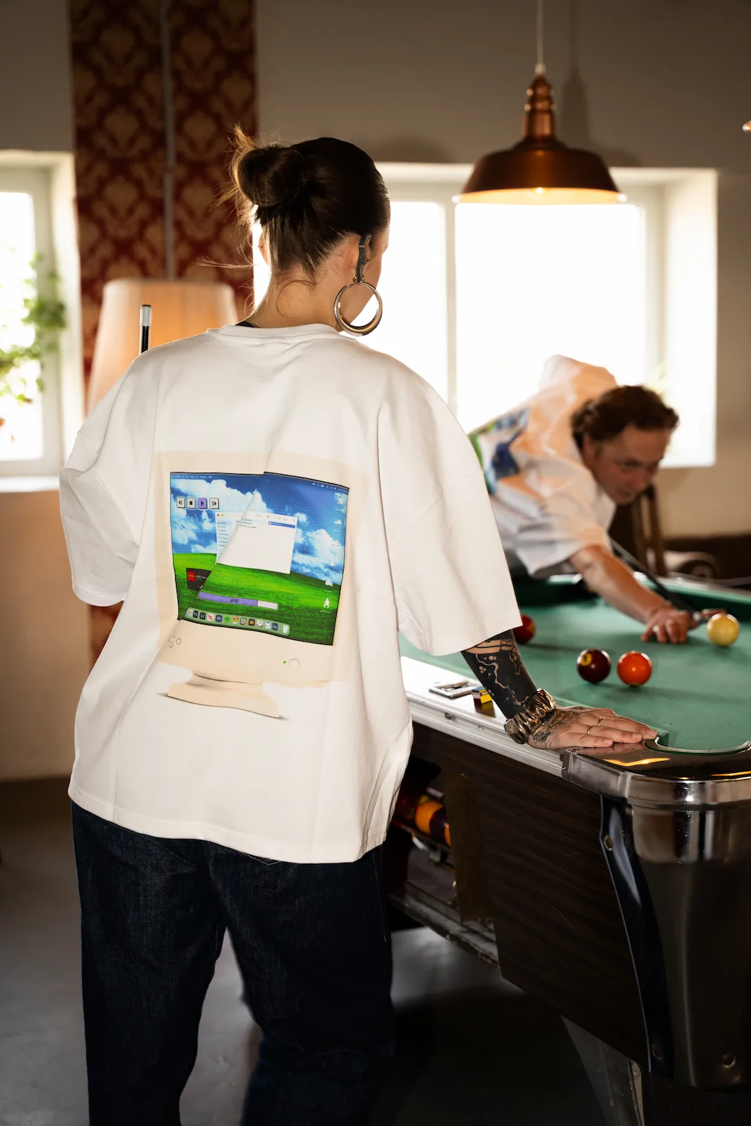 Person im GIGI and Friends Shirt neben einem Billardtisch mit grafischem Computermotiv auf dem Rücken