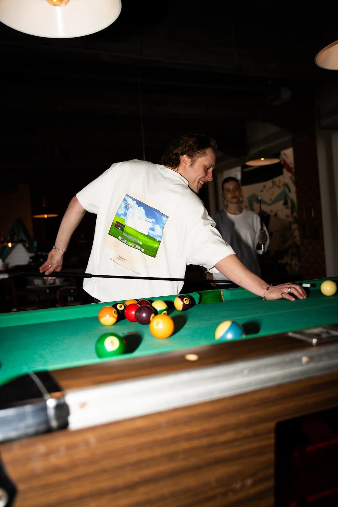 Person im GIGI and Friends Shirt beim Billardspielen mit weiteren Gästen im Hintergrund
