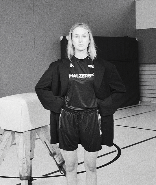 Schwarz-Weiß-Fotografie: Ein Model trägt das Malzers x GIGI Trikot in einer Sporthalle.