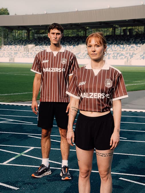 Zwei Läuferinnen und Läufer im Malzers Running Jersey auf einer Leichtathletikbahn