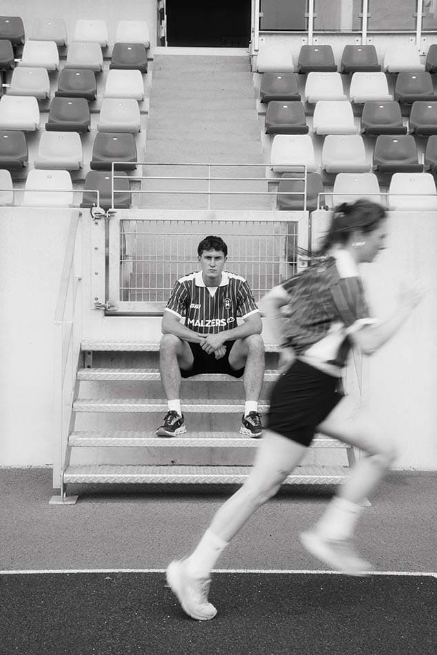 Läufer im Malzers Running Jersey auf einer Tribünentreppe während eine Läuferin vorbeiläuft